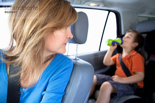 Mutter sieht zu  wie der Junge aus der Flasche auf dem Rücksitz des Autos trinkt.