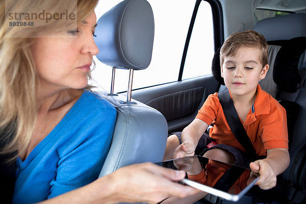 Mutter übergibt digitales Tablett an Sohn auf dem Rücksitz des Autos