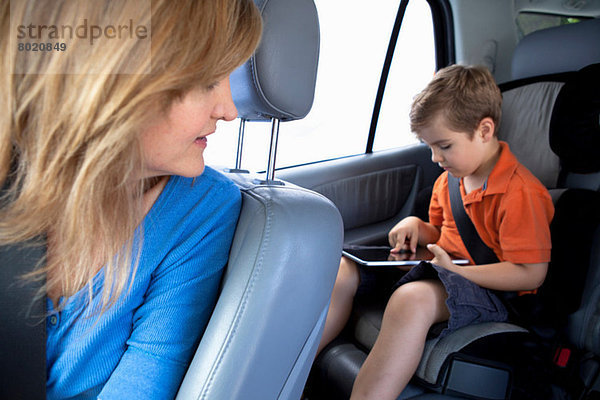 Mutter beobachtet Sohn verwenden digitale Tablette in der Rückbank des Autos