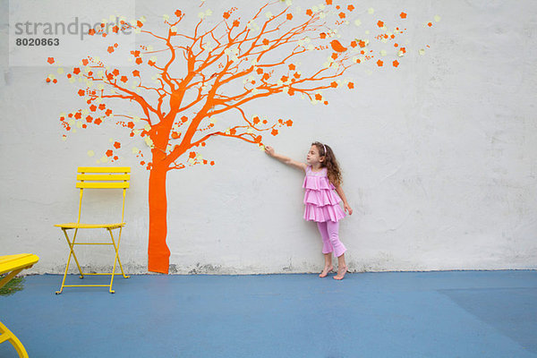 Mädchen zeigt auf Orangenbaumwand an der Wand