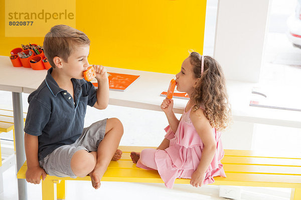 Geschwister essen Eislutscher auf der Bank im Haus