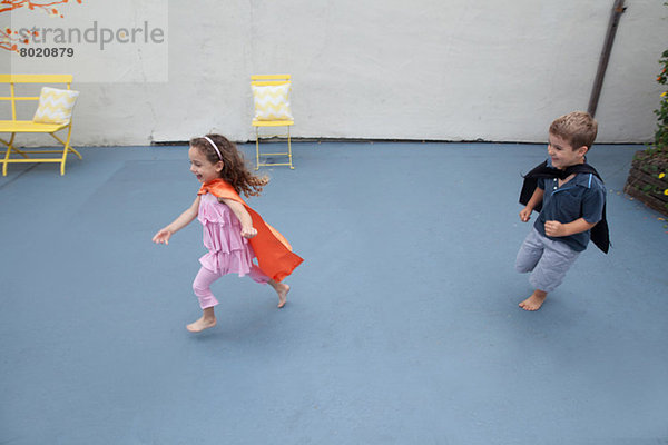 Junge und Mädchen mit Superheldenumhang spielen im Hinterhof