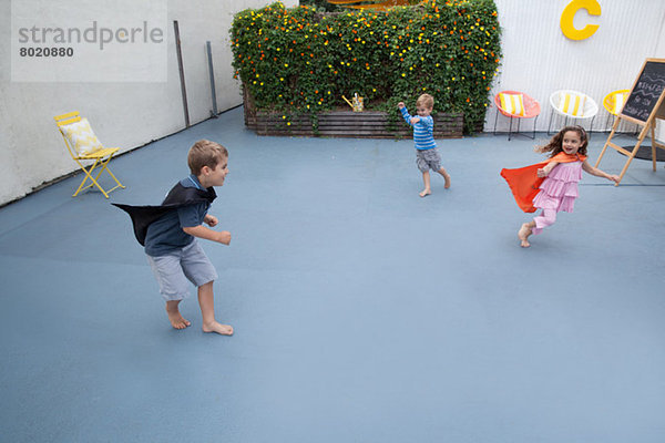 Jungen und Mädchen mit Superheldenumhang spielen im Garten.