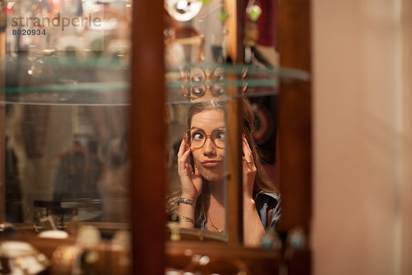 Junge Frau probiert Brille an und zieht Gesichter im Vintage-Shop