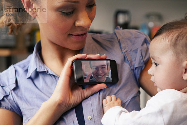 Baby Mädchen beobachtet Vater auf Videoanruf  Mutter mit Smartphone