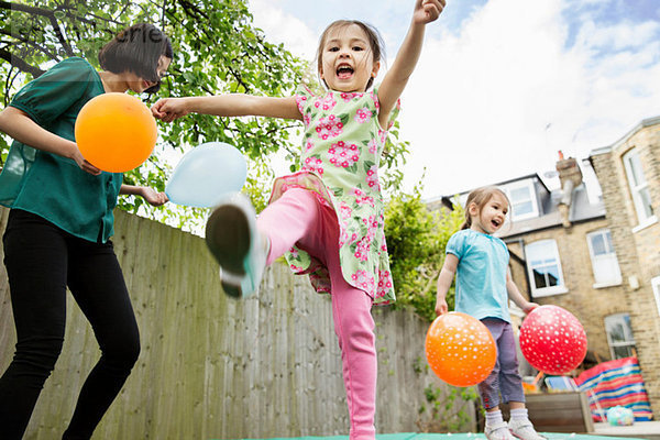 Mutter und Töchter beim Spielen im Garten mit Luftballons