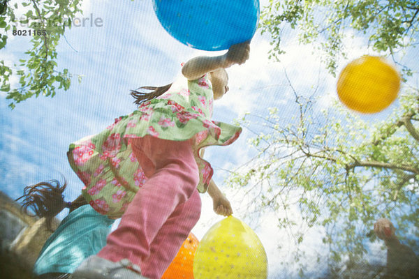 Junge Mädchen hüpfen auf Gartentrampolin mit Luftballons