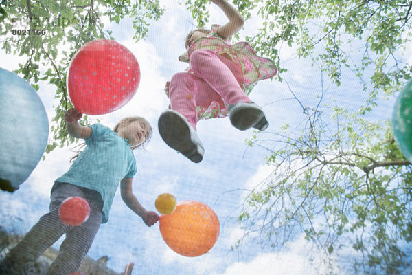 Junge Mädchen beim Springen auf Gartentrampolin mit Luftballons