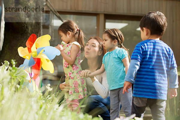 Mutter und drei Kinder mit Spielzeugwindmühle im Garten