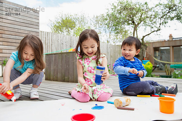 Drei kleine Kinder malen und zeichnen im Garten