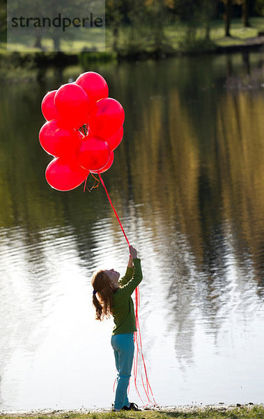 Junges Mädchen vor dem See mit roten Luftballons