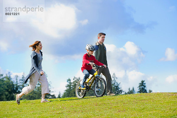 Eltern  die mit ihrem Sohn auf dem Fahrrad mithalten.
