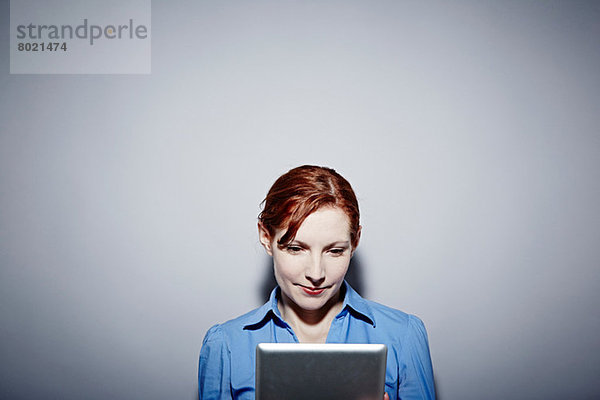 Studio-Porträt einer jungen Frau mit Blick auf das digitale Tablett