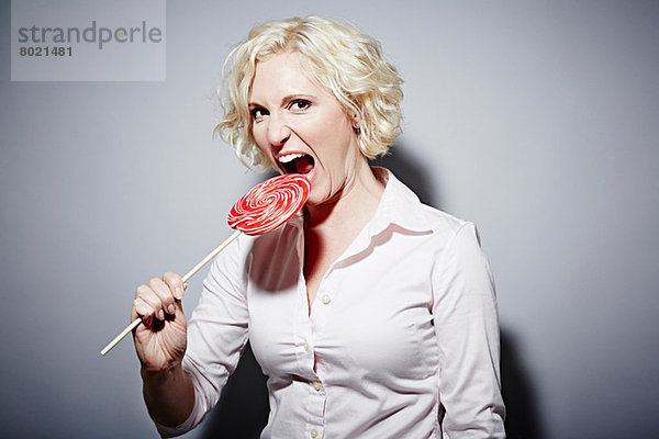Studio-Porträt einer reifen Frau  die in den roten Lolli beißt.