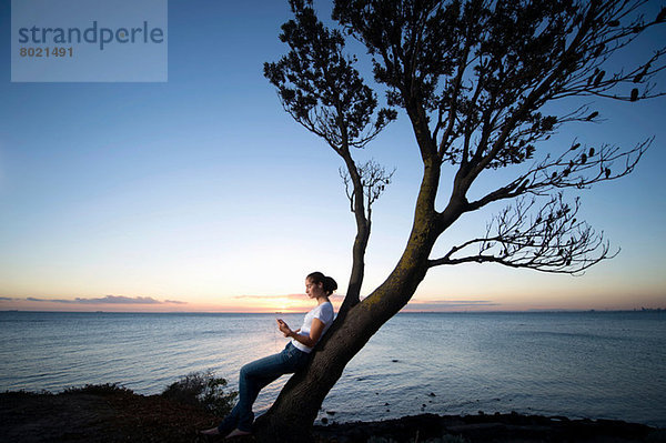 Junge Frau  die sich in der Abenddämmerung an einen Baum lehnt.