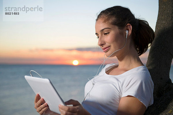 Nahaufnahme einer jungen Frau  die bei Sonnenuntergang auf ein digitales Tablett schaut.