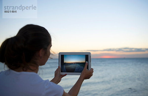 Junge Frau beim Fotografieren mit ihrem digitalen Tablett bei Sonnenuntergang