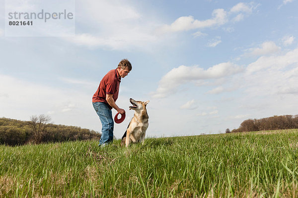 Mann trainiert Elsässer Hund mit rotem Frisbee