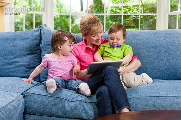 Großmutter und Enkelkinder auf dem Sofa beim Betrachten des digitalen Tabletts
