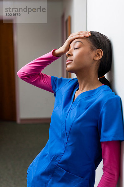 Krankenschwester mit geschlossenen Augen und Hand auf Kopf im Krankenhausflur