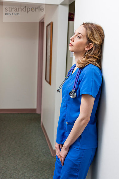 Krankenschwester in blauem Kittel in Anlehnung an die Wand im Krankenhausflur