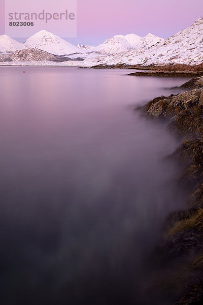 Fjord mit Steinen und Bergkette im Abendlicht