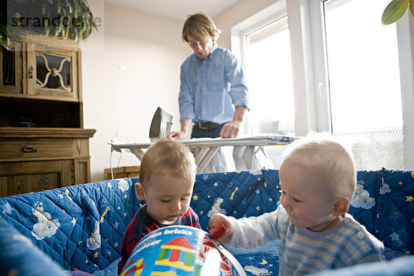 Junger Vater bei der Hausarbeit während seine Söhne im Laufgitter spielen