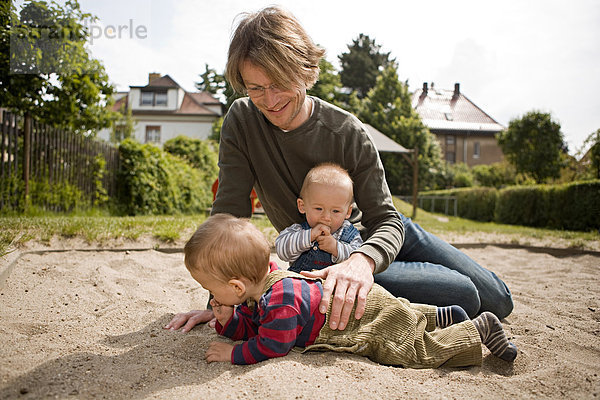 Junger Vater mit zwei kleinen Kindern spielt auf einem Spielplatz