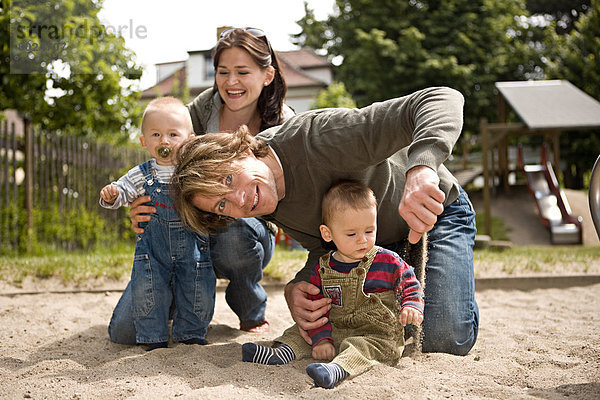 Junge Familie mit zwei kleinen Kindern spielt auf einem Spielplatz