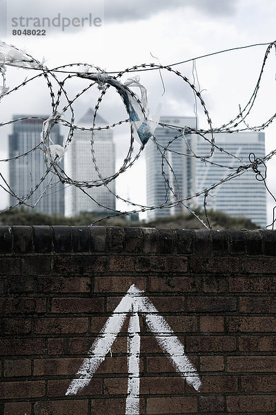 Ziegelmauer mit Stacheldraht auf der Oberseite  Plastiktaschen gefangen auf Widerhaken  Canary Wharf im Hintergrund  Greenwich-Halbinsel  London  Großbritannien