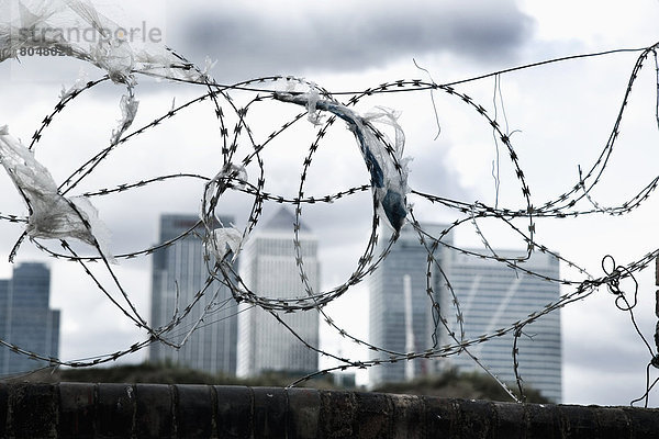 Ziegelmauer mit Stacheldraht auf der Oberseite  Plastiktaschen gefangen auf Widerhaken  Canary Wharf im Hintergrund  Greenwich-Halbinsel  London  Großbritannien