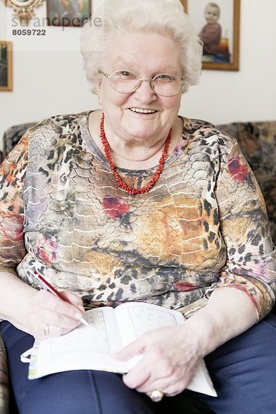 Lächelnde alte Frau mit Brille schreibt