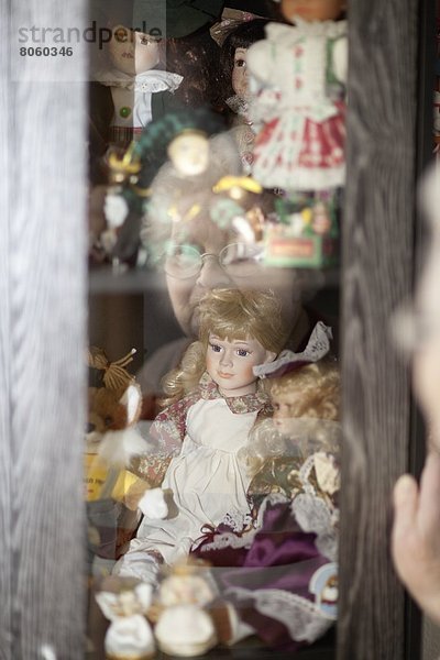 Alte Frau schaut auf Puppen in einer Vitrine