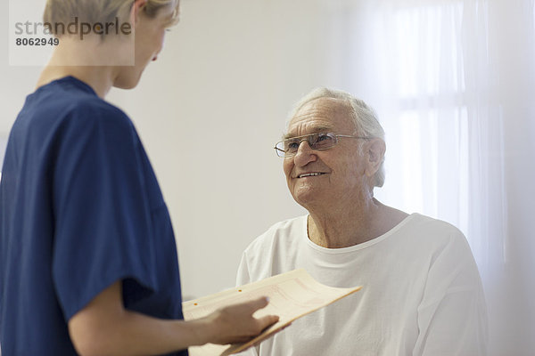 Krankenschwester im Gespräch mit älterem Patienten im Krankenhauszimmer
