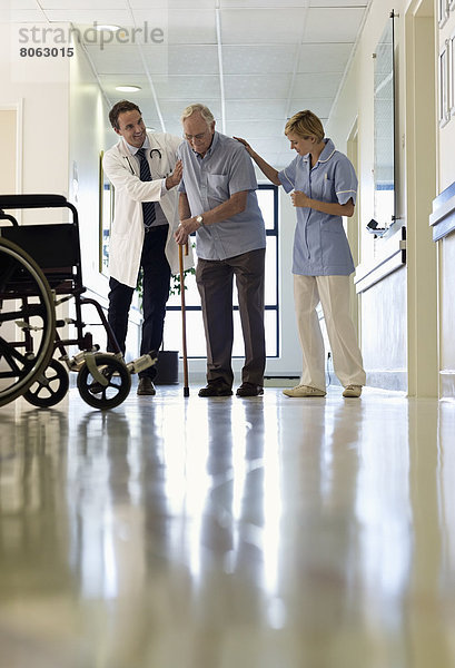 Arzt und Krankenschwester helfen älteren Patienten beim Gehen im Krankenhaus