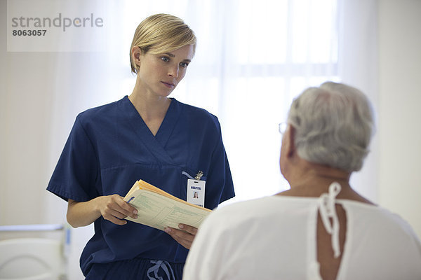 Krankenschwester und älterer Patient sprechen im Krankenhauszimmer