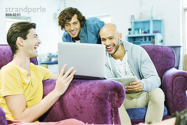 Männer  die den Laptop zusammen im Wohnzimmer benutzen