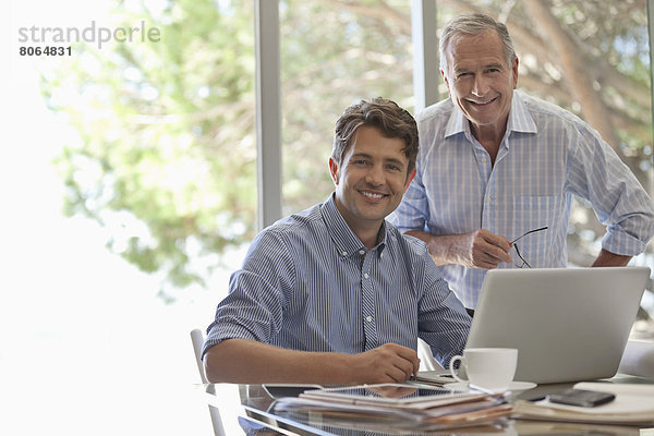 Älterer Mann und jüngerer Mann lächeln zusammen am Schreibtisch