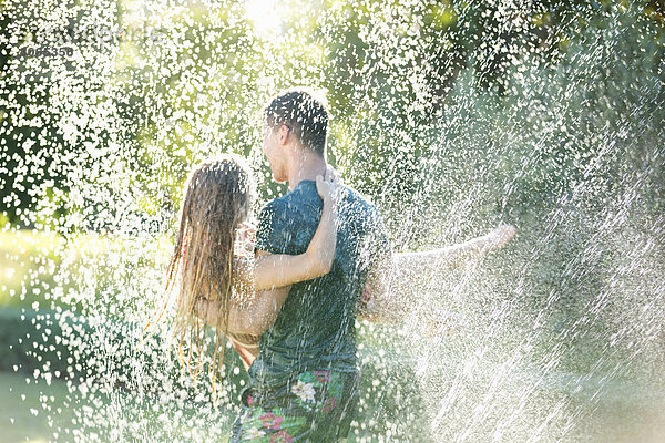 Paar spielt im Sprinkler im Hinterhof