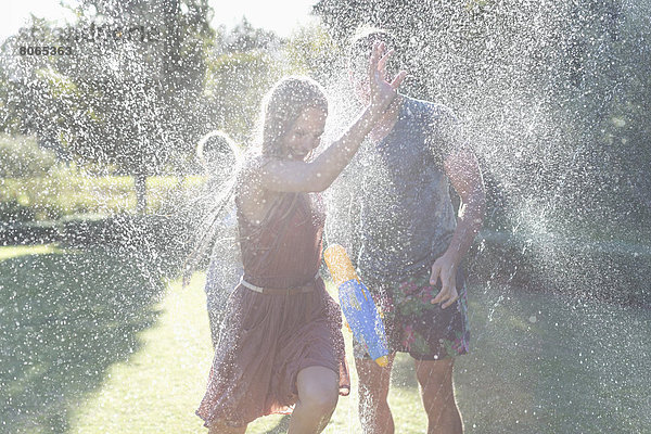 Paar spielt im Sprinkler im Hinterhof