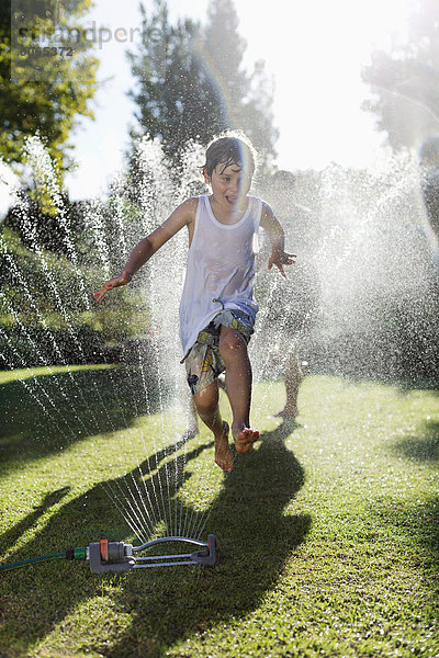 Junge spielt im Sprinkler im Hinterhof
