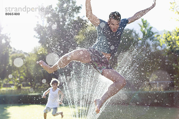 Vater und Sohn spielen im Sprinkler im Hinterhof