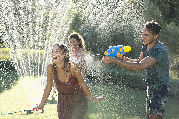 Freunde spielen mit Wasserpistolen im Sprinkler im Hinterhof