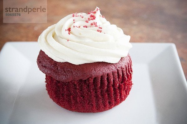 Red Velvet Cupcake mit weißem Zuckerguss und roten Zuckerkristallen