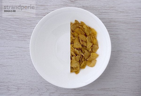 Halbierte Portion Cornflakes in weißer Schale (Aufsicht)