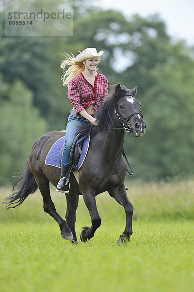 Junge Frau steht reitet auf einem Pferd auf einer Wiese