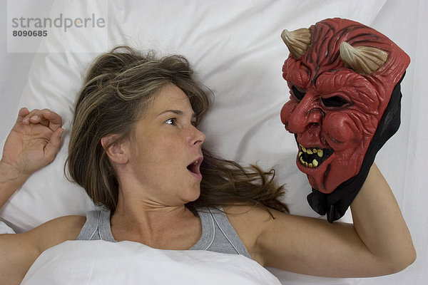 Frau liegt im Bett  Teufelsmaske