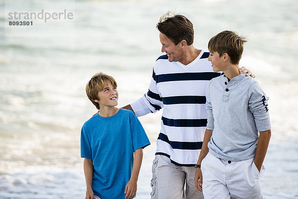 Caucasian father and sons walking on beach