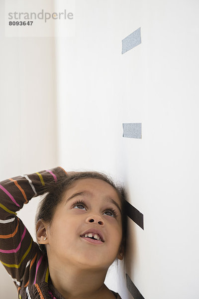 Hispanic girl measuring her height on wall