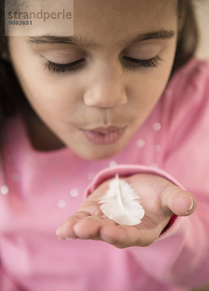 Hispanic girl blowing on feather